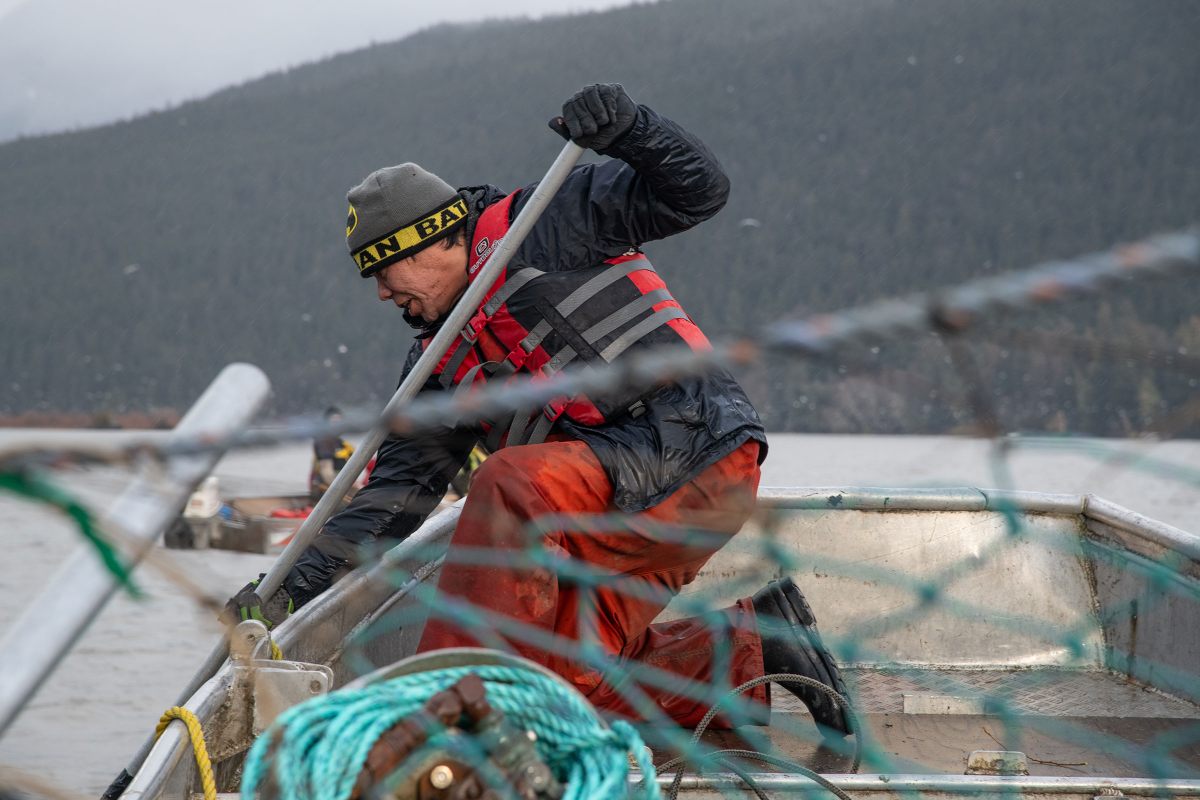 Nisg̱a’a fisherman Peter Smith struggles to push a log away from the hull of a fishing skiff during an evening of eulachon harvesting on the Nass.