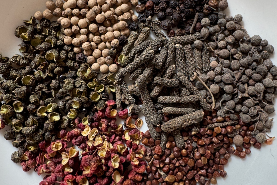 Clockwise from top left: white, black, long, cubeb, grains of paradise, red Sichuan, and green Sichuan peppers. 